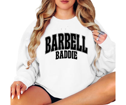 A woman wearing a white crewneck sweatshirt with 'BARBELL BADDIE' printed in black arched text across the chest, shown against a plain white background.