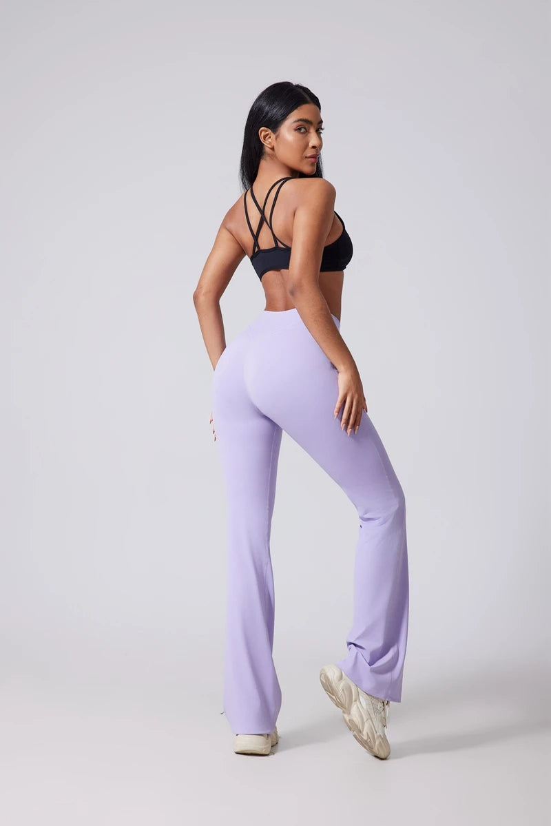 Woman wearing a black sports bra and lavender leggings on a white background..