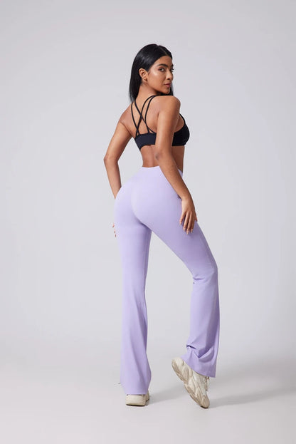 Woman wearing a black sports bra and lavender leggings on a white background..