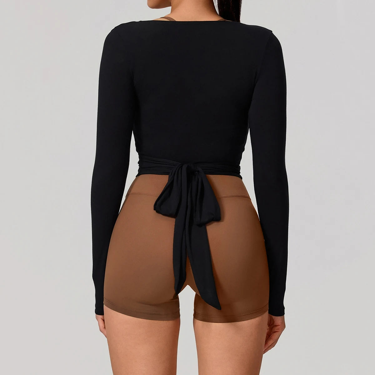 Person wearing a black long-sleeve top and brown shorts on a plain background