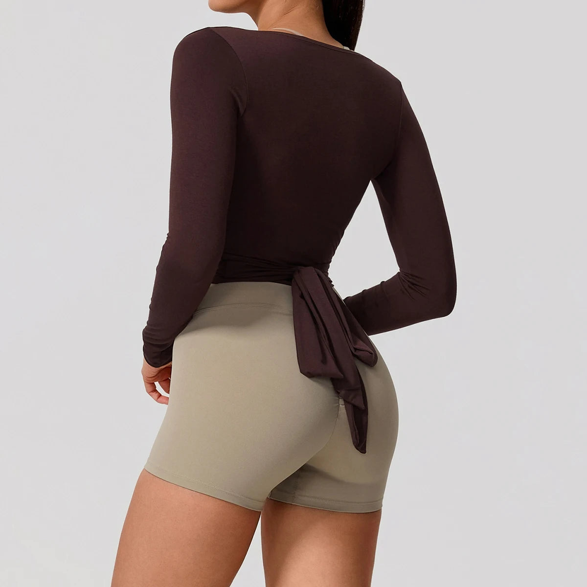 Person wearing a brown long-sleeve top and beige shorts on a plain background