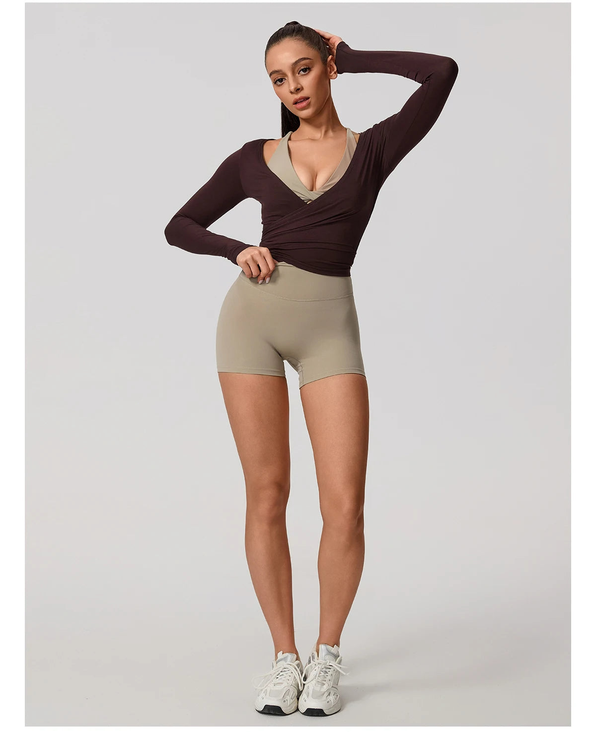 Woman wearing a brown long-sleeve top and beige shorts on a white background
