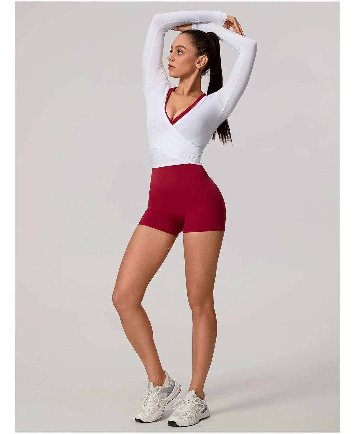 Woman wearing a white long-sleeve top and red shorts on a gray background