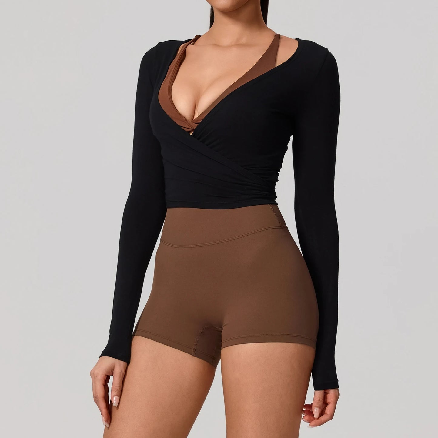 Person wearing a black long-sleeve top and brown shorts on a gray background