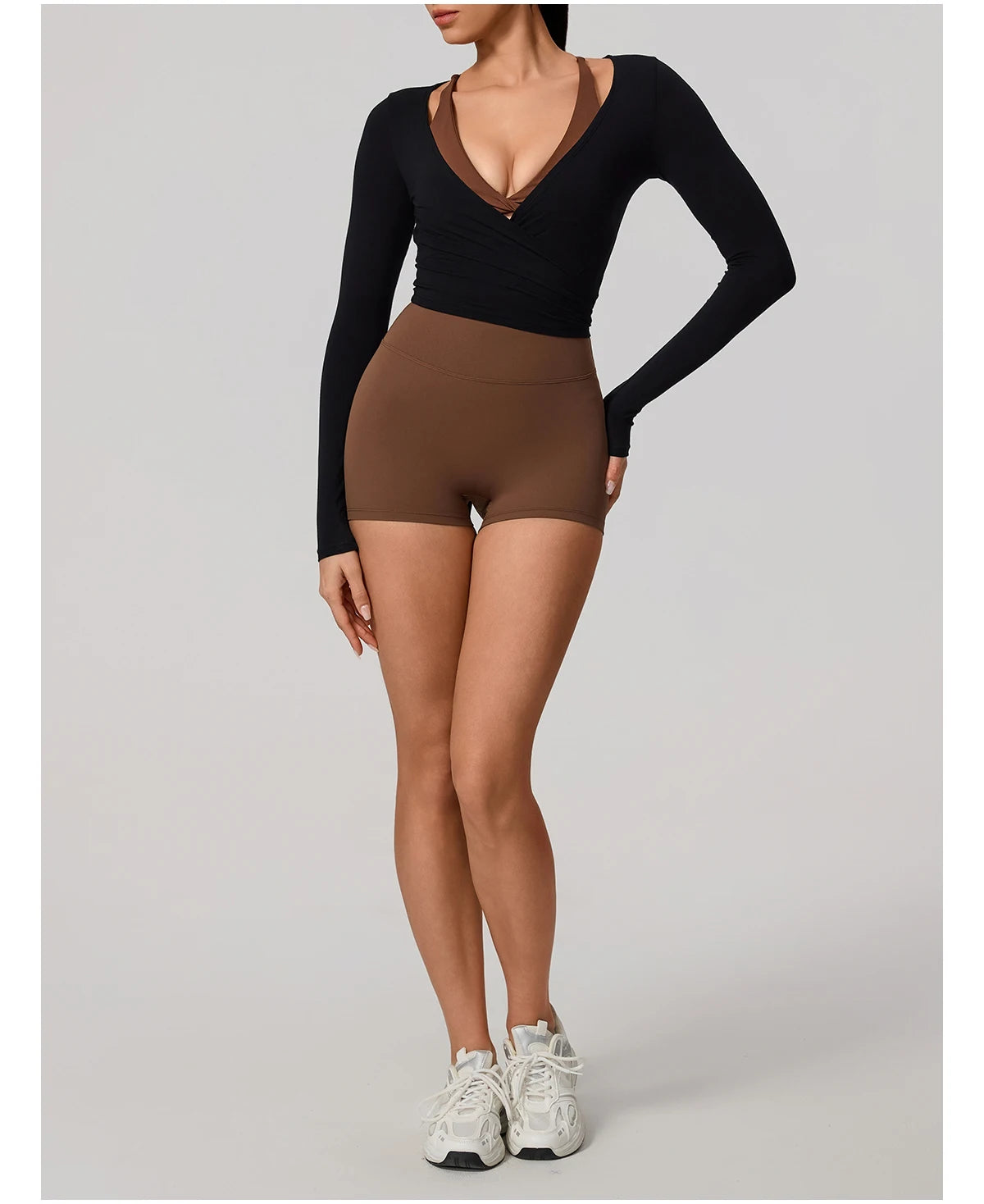 Person wearing a black long-sleeve top and brown high-waisted shorts on a gray background