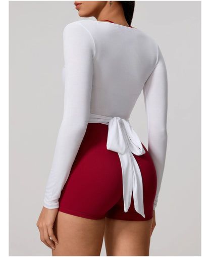 Person wearing a white long-sleeve top and red shorts with a white bow on a light gray background
